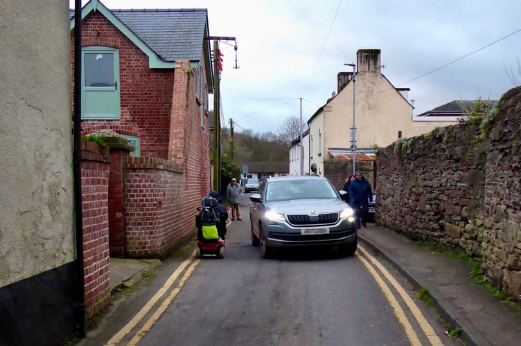 A car drives down Goldwire Lane past a mobility scooter