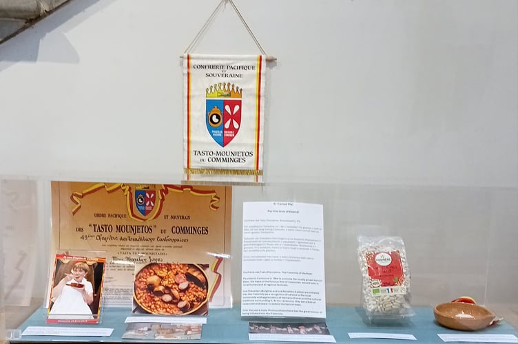 Cassoulet as featured in the exhibition ﻿showing Twinning Chair, Marilyn Jones, eating a dish of cassoulet as she is initiated into the Tastos Mounjetos order - a brotherhood committed to promote the Cassoulet. Her membership certificate is behind her.
