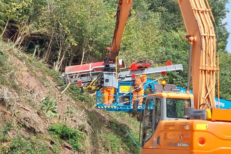 A drilling rig mounted on a long reach excavator inserts test nails into the rockface to confirm that the materials and method are suitable